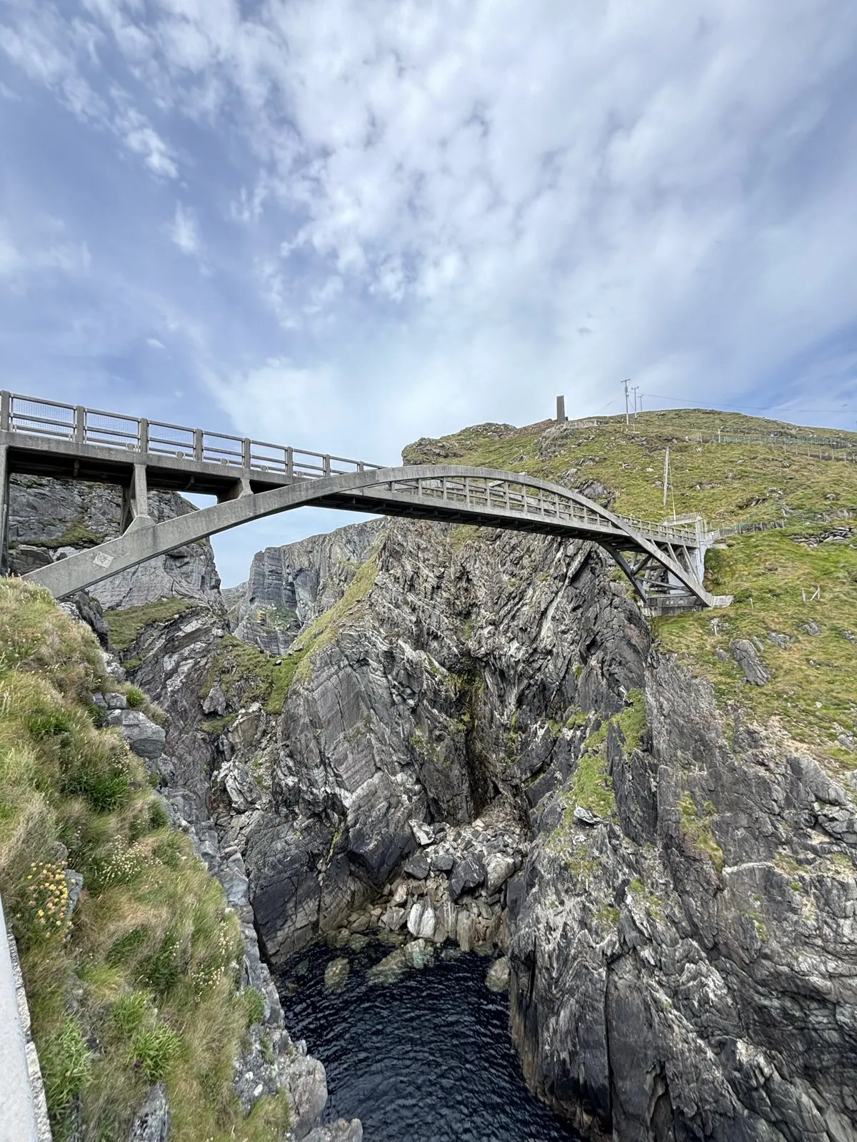 Concrete footbridge spanning across a deep rocky coastal sea gorge.