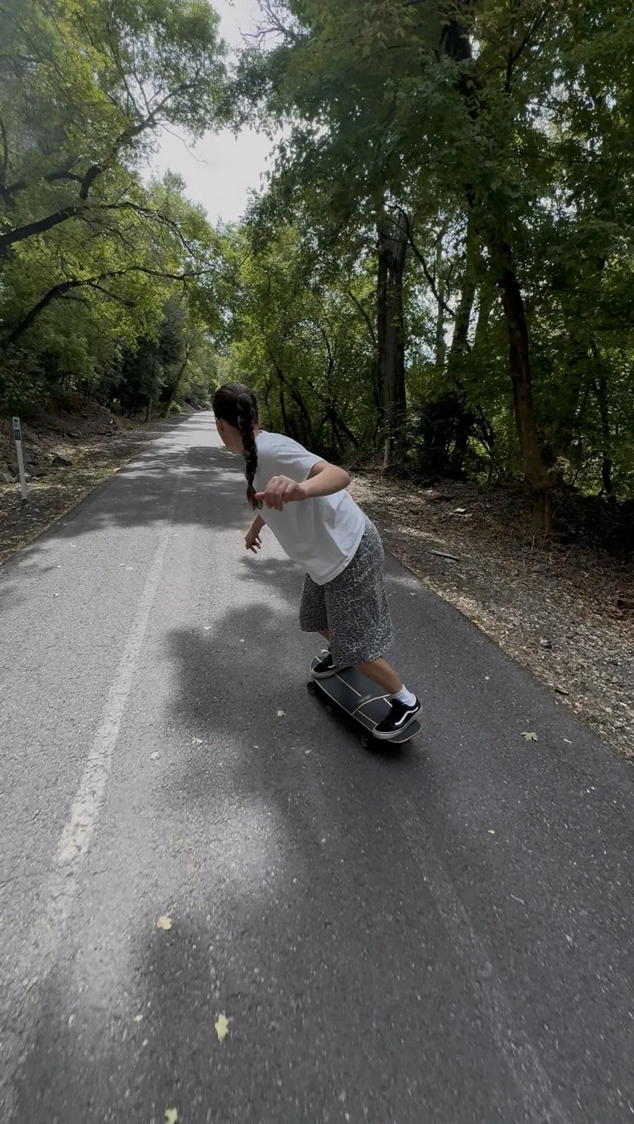 A person skateboarding down a paved forest path.