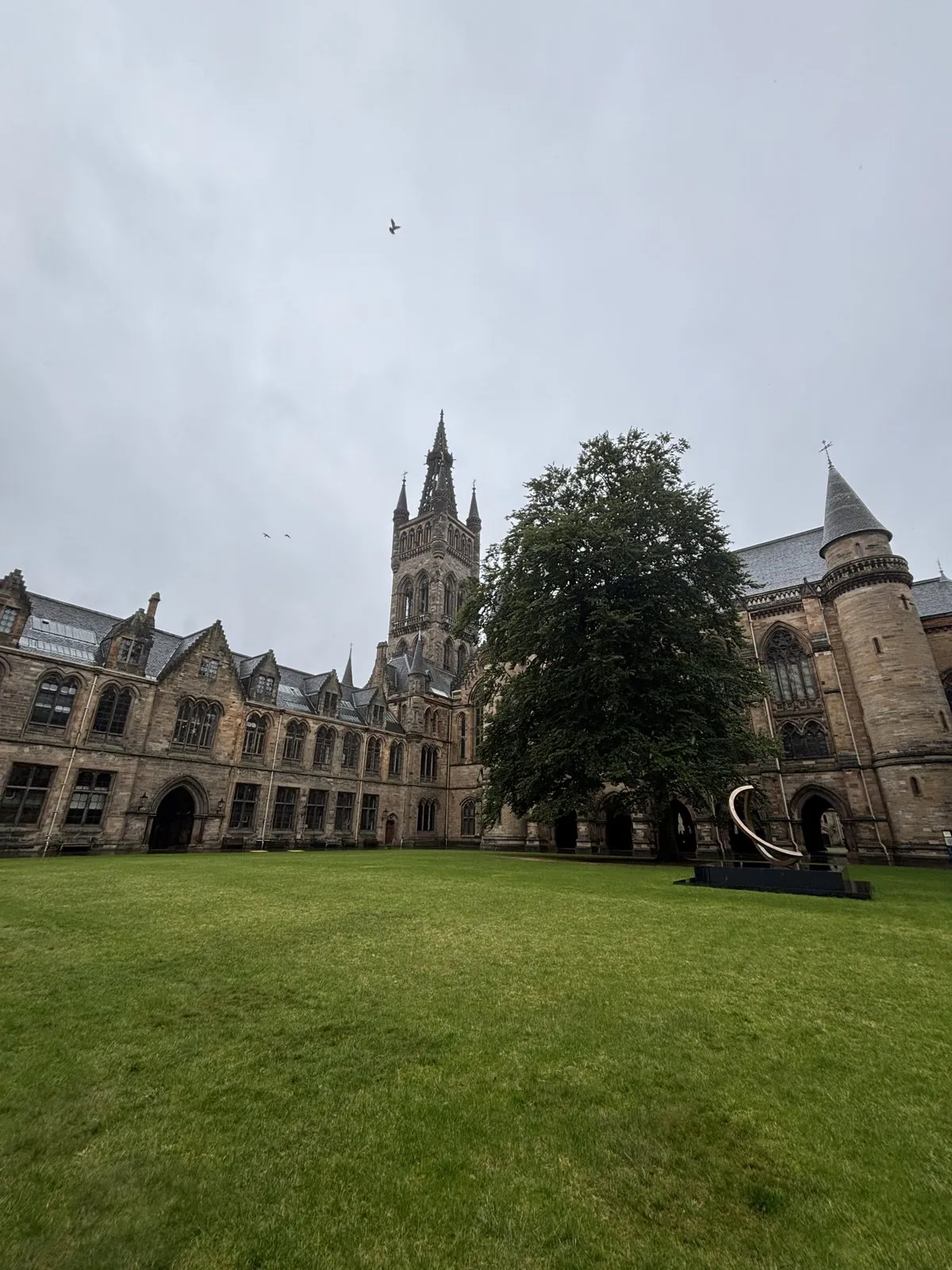 Gothic stone architecture overlooking an open green courtyard under an overcast sky.