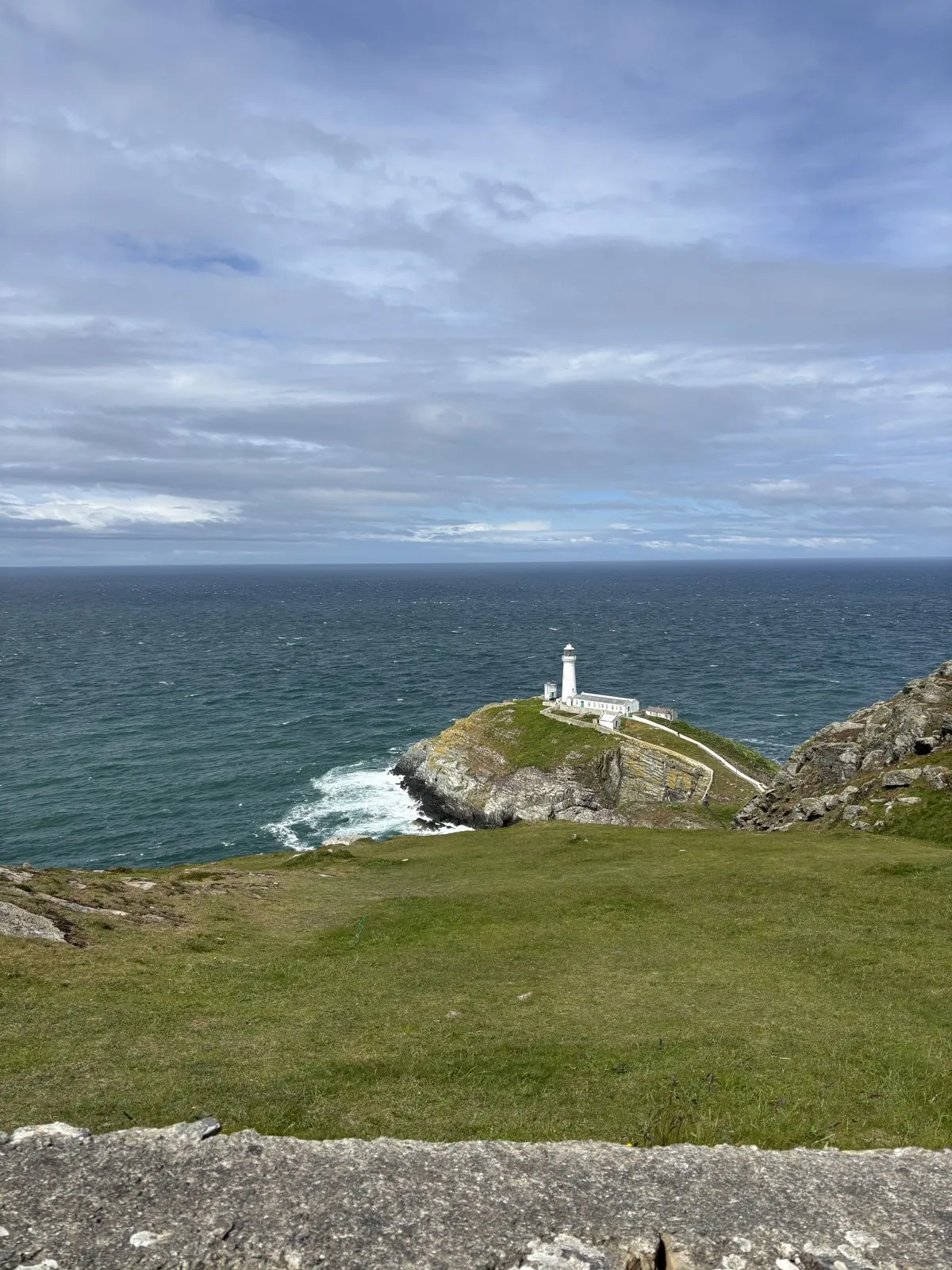 White lighthouse situated on a rocky coastal headland against deep blue sea.