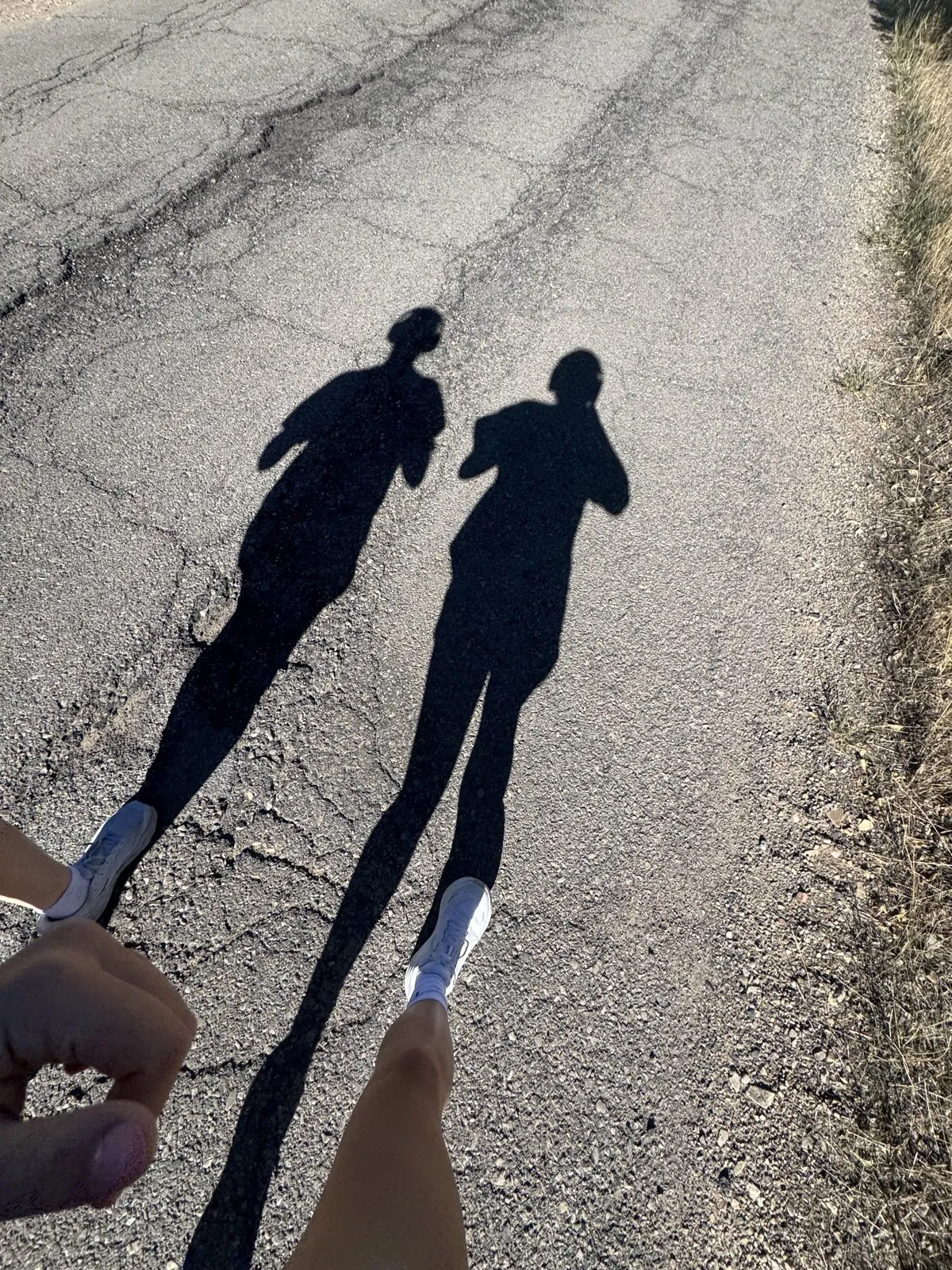 The long shadows of two runners cast across an asphalt road surface.