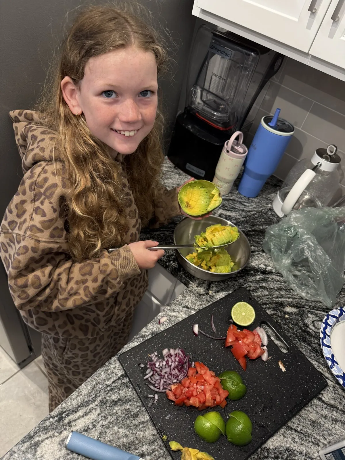 Preparation of fresh guacamole with sliced limes, tomatoes, red onion, and avocado.